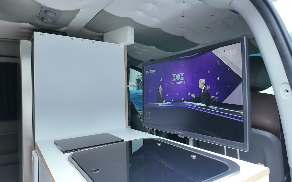 캠핑스타 승합차 캠핑카 실내. 싱크대 옆에 TV가 세워져 있다.