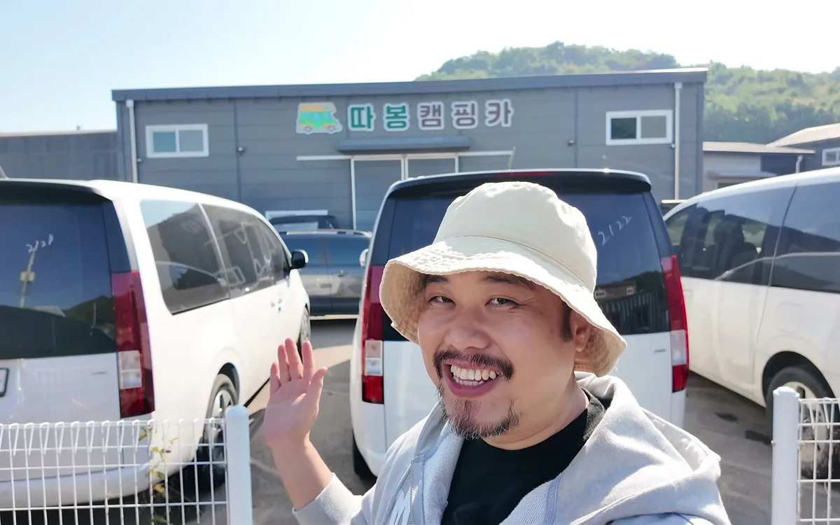 따봉캠핑카 매장 앞에서 손을 흔들며 활짝 웃는 진행자 나그네.